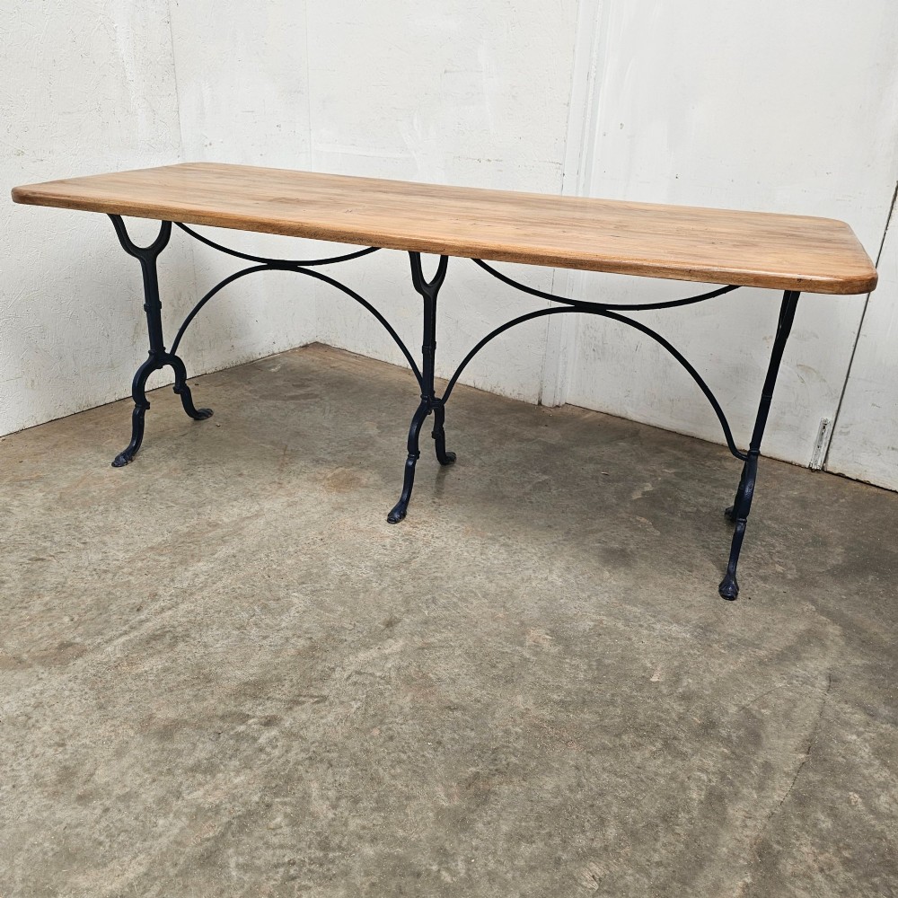 A long rectangular light elm wood table top supported by three curved black iron legs with arching stretchers.