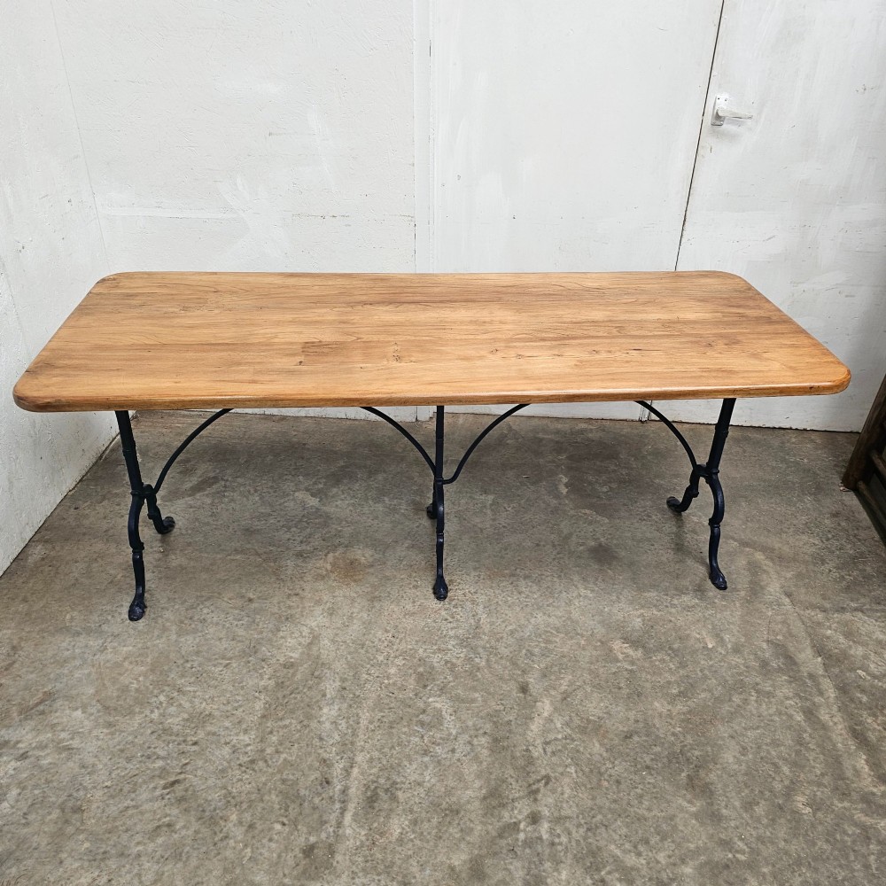 A long rectangular light elm wood table top supported by three curved black iron legs with arching stretchers. View V
