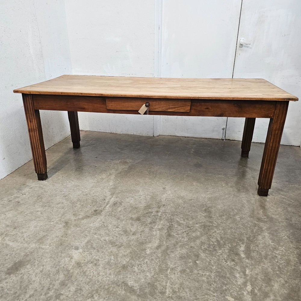 A rectangular French fruitwood dining table featuring a central frieze drawer with a wooden knob and fluted tapered legs.