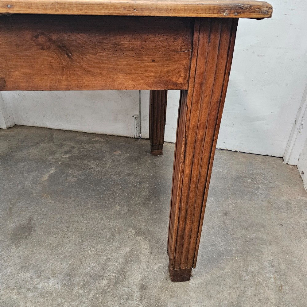 A rectangular French fruitwood dining table featuring a central frieze drawer with a wooden knob and fluted tapered legs. View III