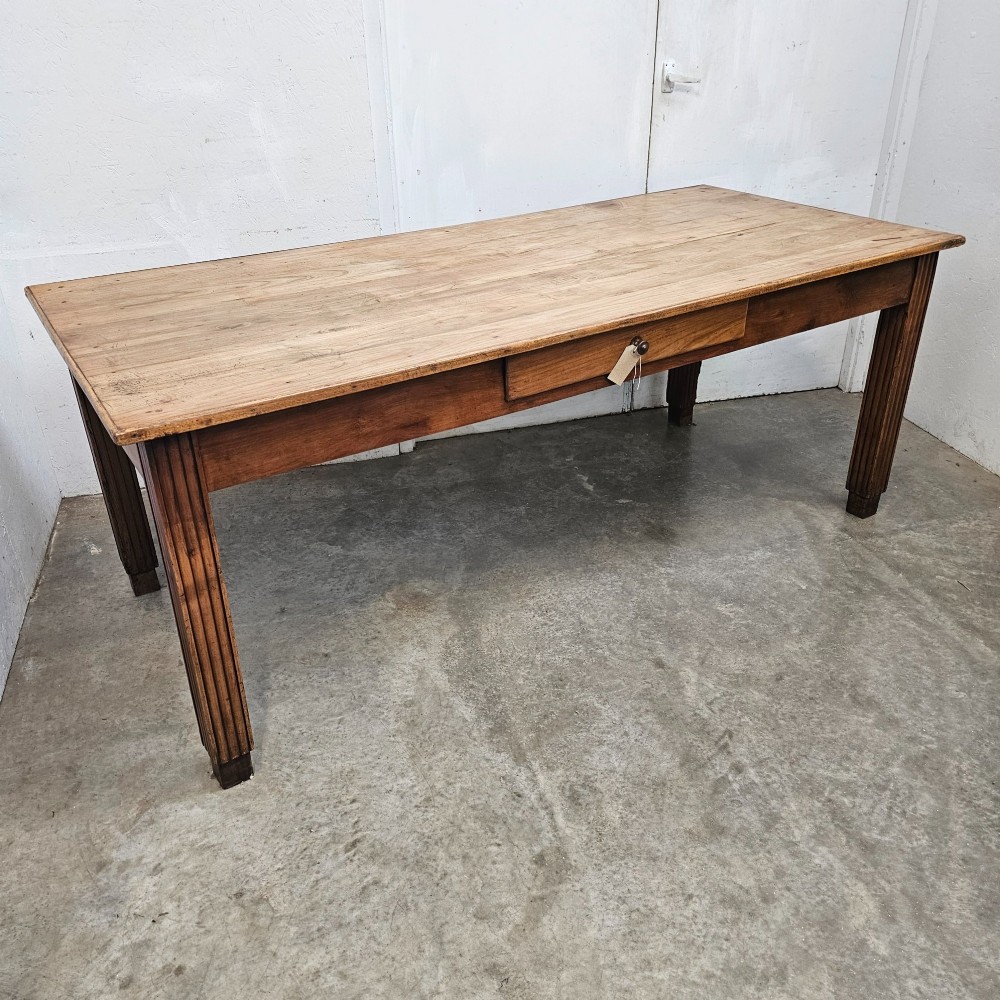 A rectangular French fruitwood dining table featuring a central frieze drawer with a wooden knob and fluted tapered legs. View V