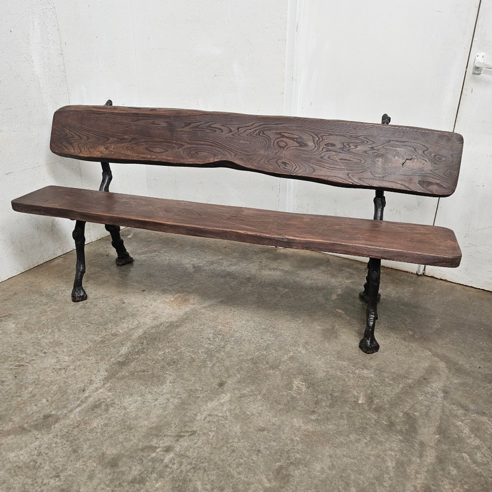 A rustic French garden bench featuring a dark elm slab seat and backrest supported by black cast iron legs designed to resemble natural tree branches.