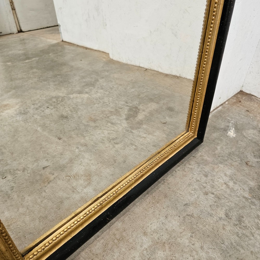 A rectangular French Louis Philippe mirror featuring rounded upper corners, an ebonised black outer frame, and a beaded gold leaf inner trim. View IV