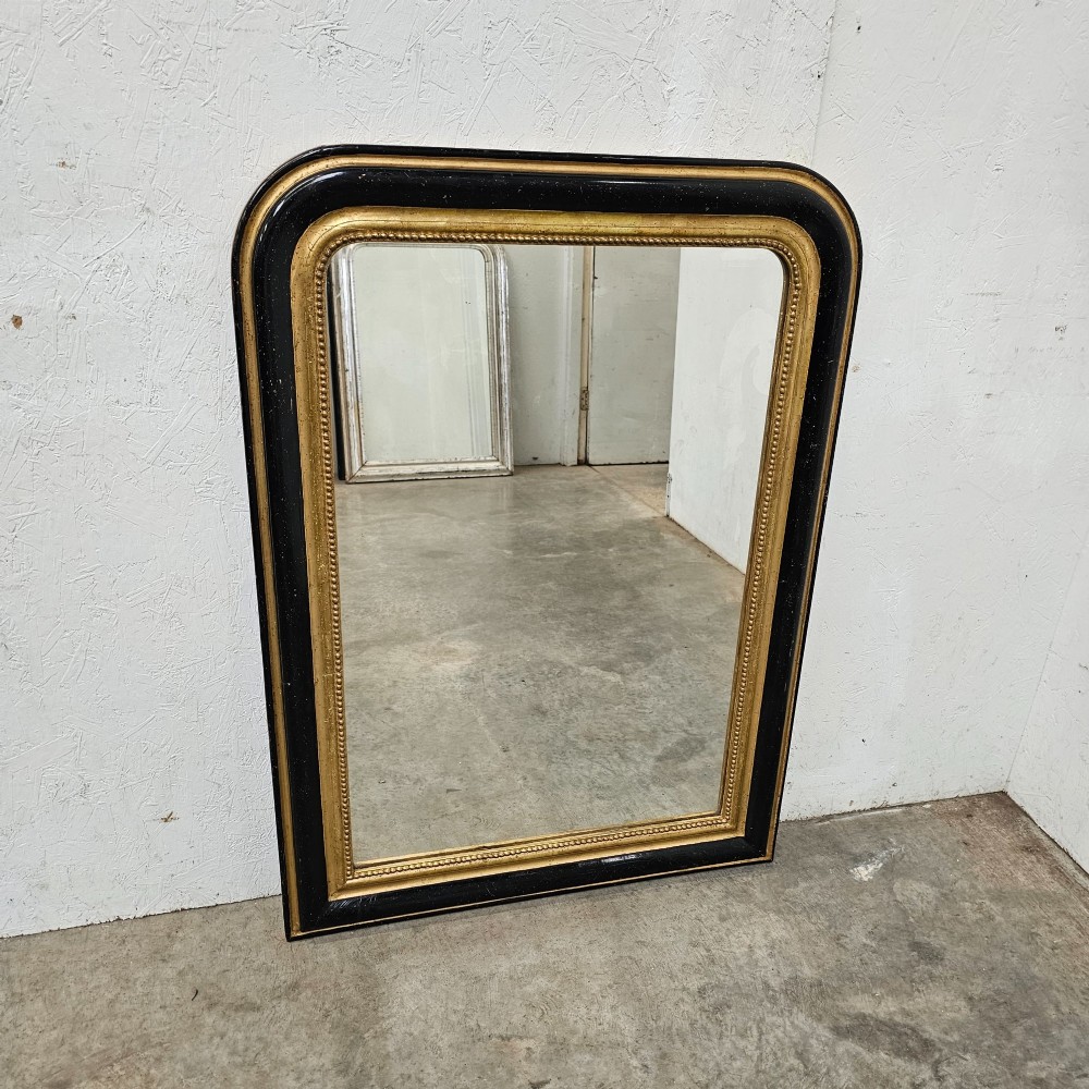 A rectangular French Louis Philippe mirror featuring rounded upper corners, an ebonised black outer frame, and a beaded gold leaf inner trim.