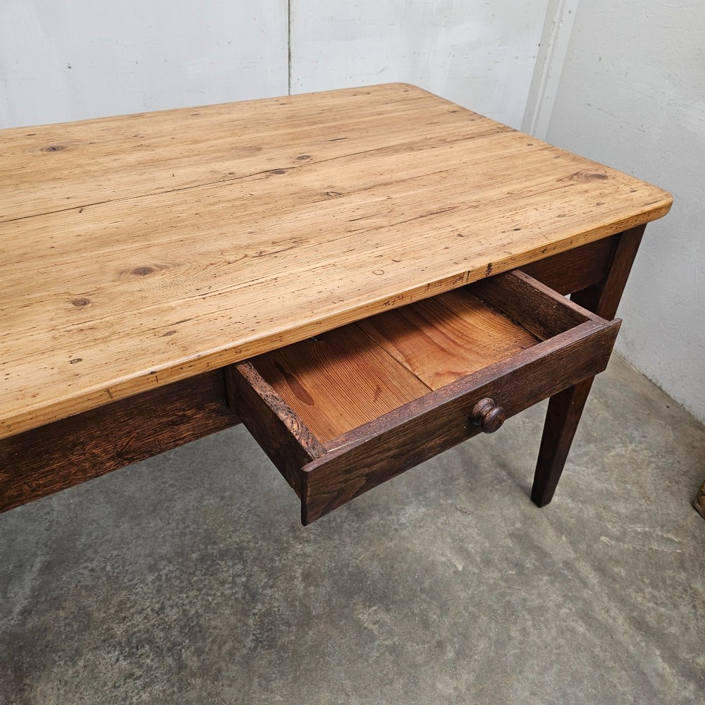An antique French farmhouse dining table with a light pine plank top, two apron drawers, and a dark oak frame with tapered legs. View V