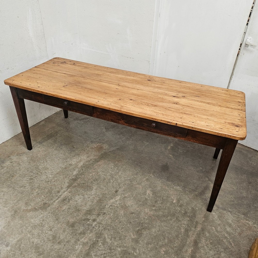An antique French farmhouse dining table with a light pine plank top, two apron drawers, and a dark oak frame with tapered legs. View VI