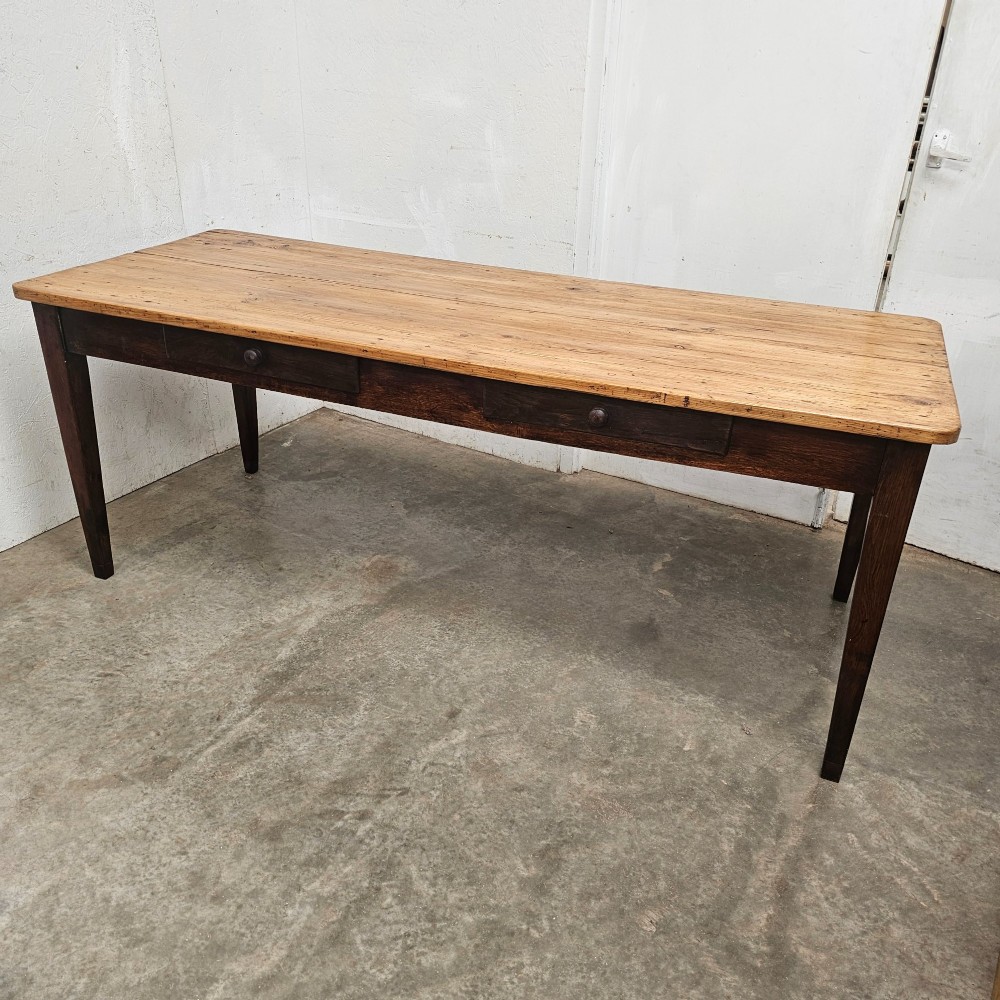 An antique French farmhouse dining table with a light pine plank top, two apron drawers, and a dark oak frame with tapered legs.