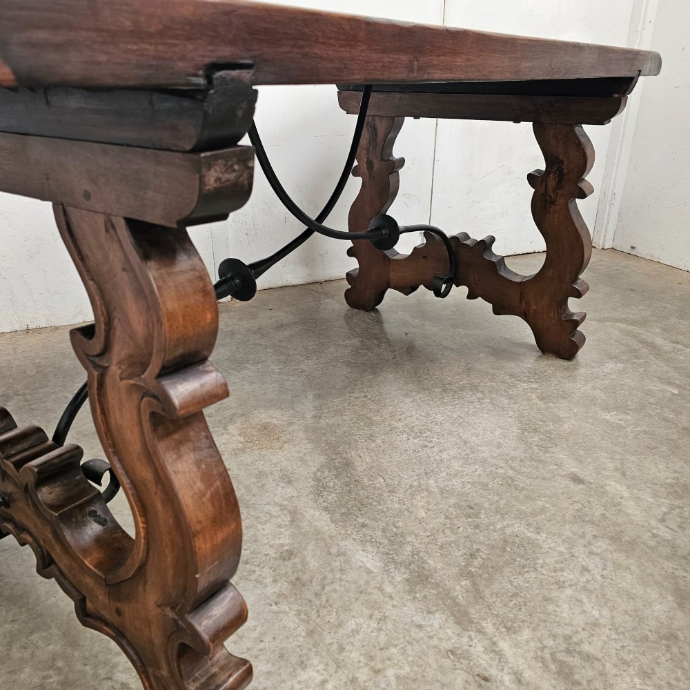 A dark brown rectangular wooden dining table with carved trestle legs connected by curved wrought iron stretchers. View II