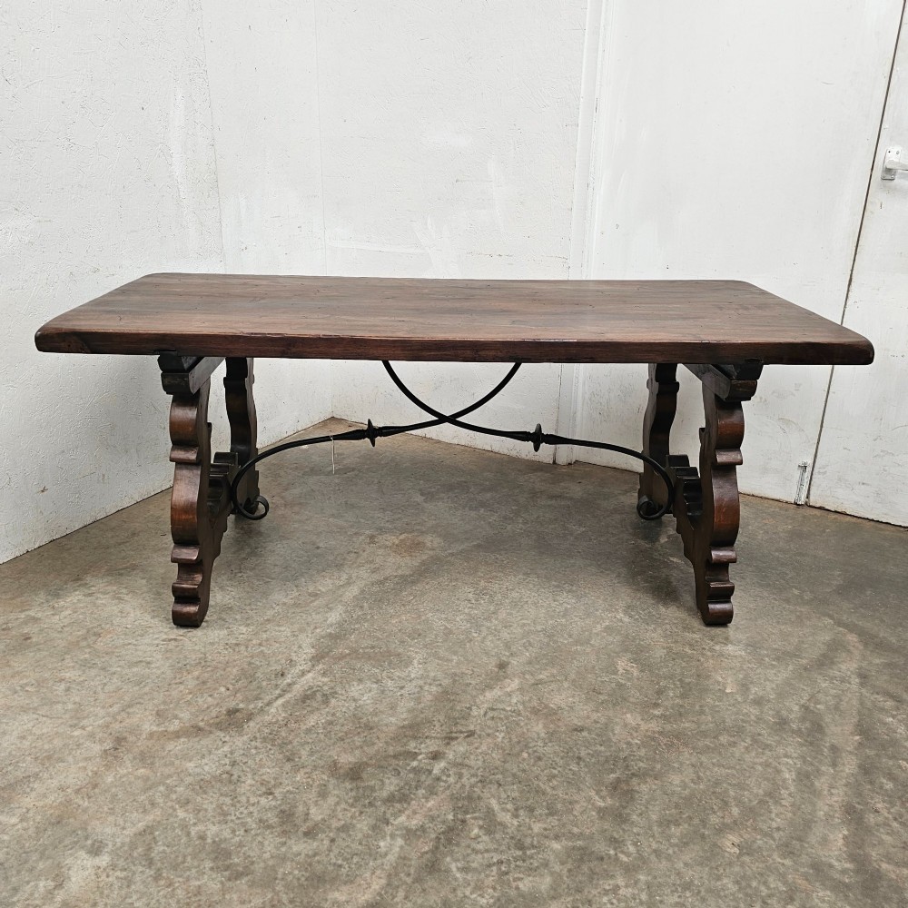 A dark brown rectangular wooden dining table with carved trestle legs connected by curved wrought iron stretchers.