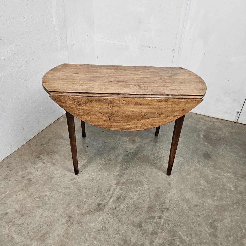 An antique wooden French drop-leaf table with semi-circular side leaves folded down and four tapered wooden legs. View II