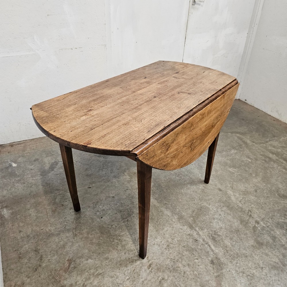An antique wooden French drop-leaf table with semi-circular side leaves folded down and four tapered wooden legs. View IV