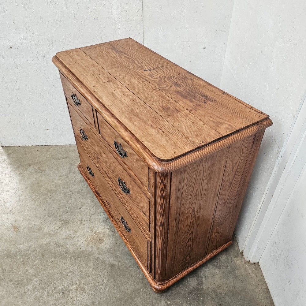 A Victorian pitch pine chest of drawers featuring a two-over-two drawer layout with brass drop handles and a visible wood grain. View V