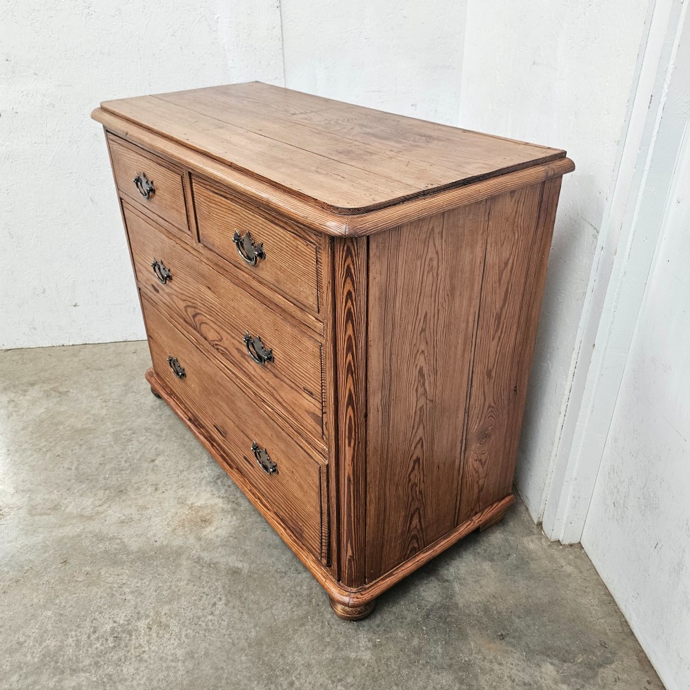 A Victorian pitch pine chest of drawers featuring a two-over-two drawer layout with brass drop handles and a visible wood grain. View VI