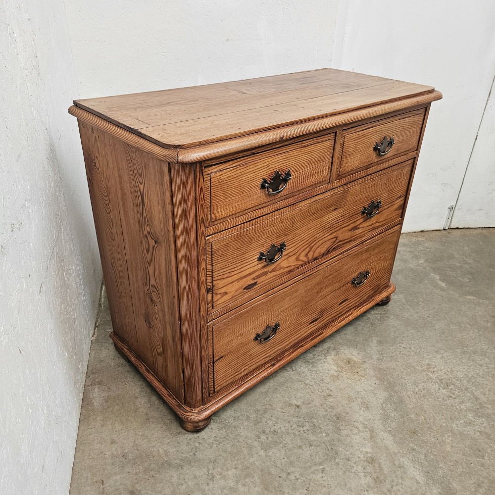 A Victorian pitch pine chest of drawers featuring a two-over-two drawer layout with brass drop handles and a visible wood grain. View VII