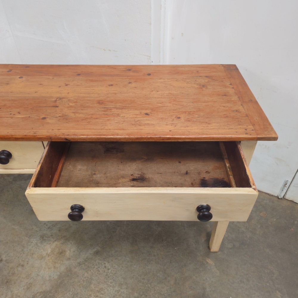 A nineteenth-century English painted pine dairy table with a natural timber top, a cream painted base, double drawers, and dark turned wooden knobs. View II