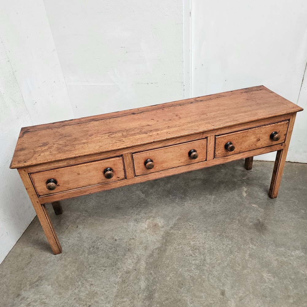 An English country pine and elm dresser base featuring a planked top, three frieze drawers with turned knobs, and four square tapered legs. View II