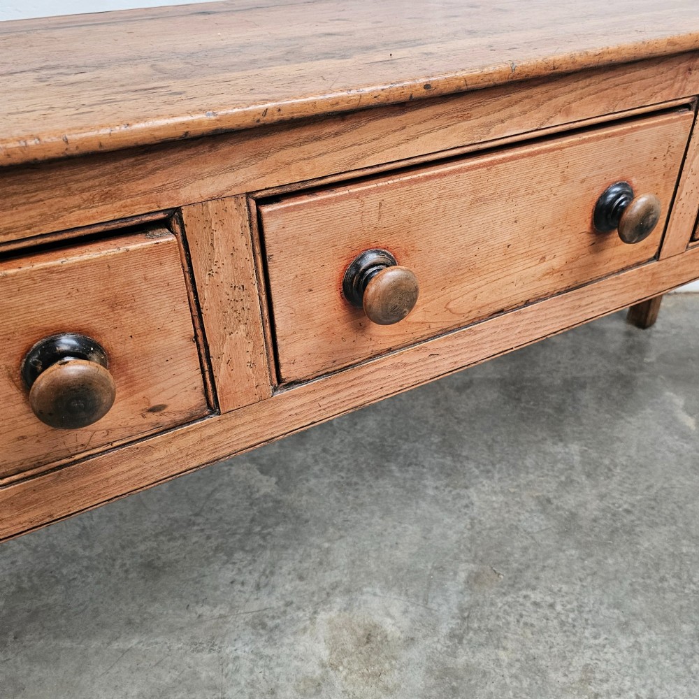 An English country pine and elm dresser base featuring a planked top, three frieze drawers with turned knobs, and four square tapered legs. View IV