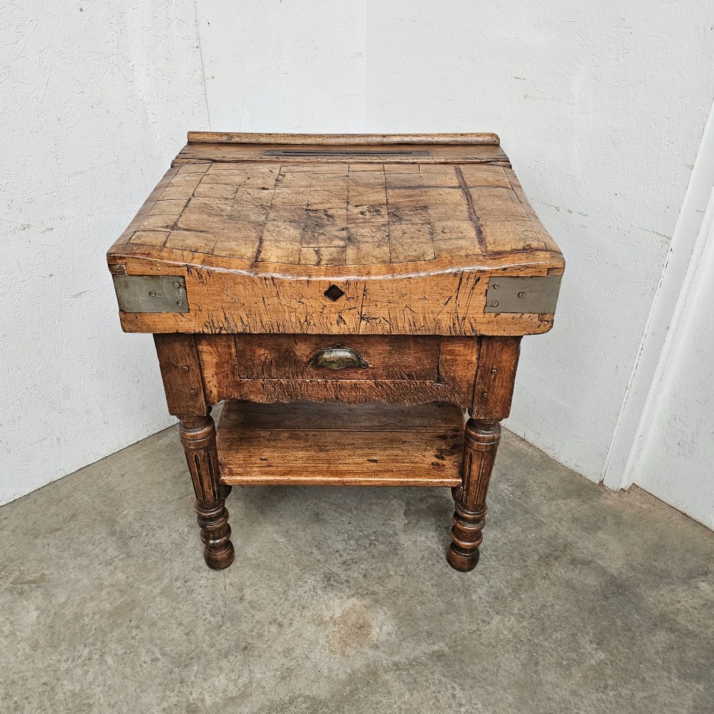 A French beechwood butchers block featuring a thick end-grain top with metal corner brackets, a single drawer with a cup handle, a lower shelf, and turned legs. View V