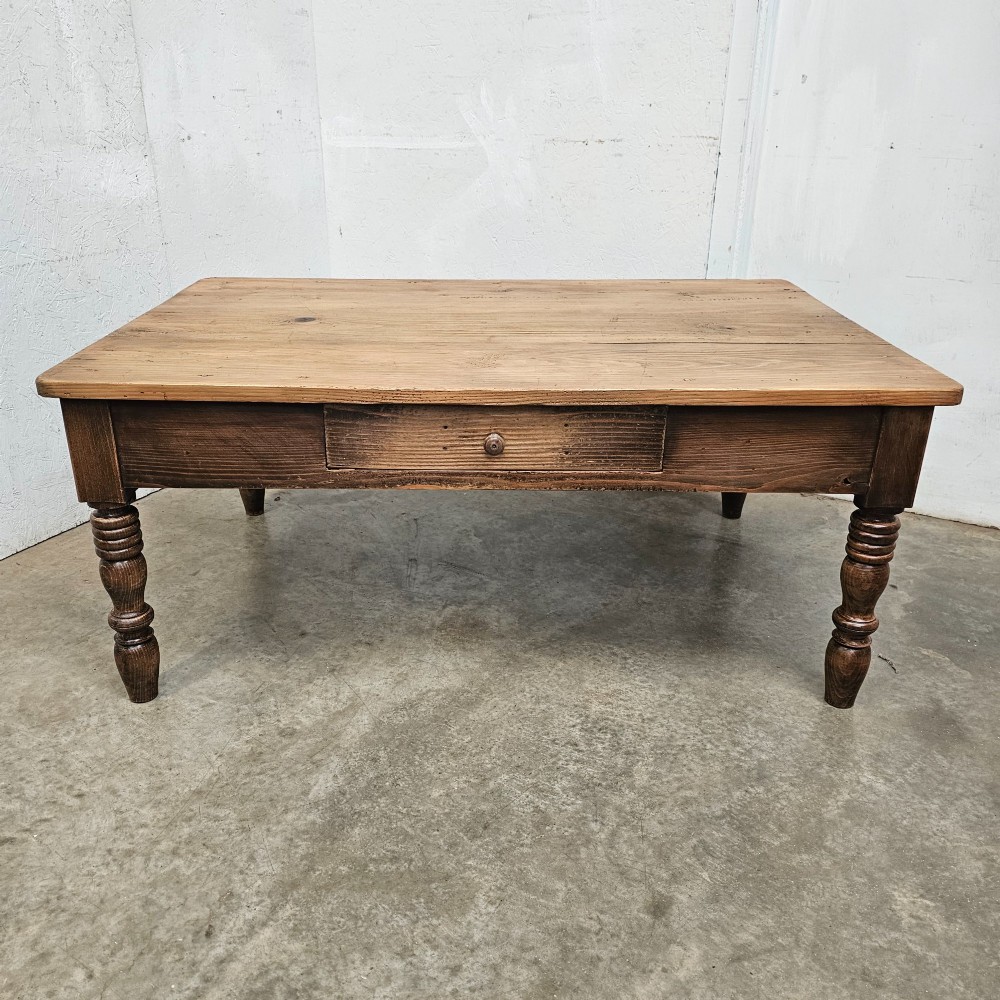 A rectangular rustic pine coffee table featuring four turned legs and a single central frieze drawer with a round wooden knob.