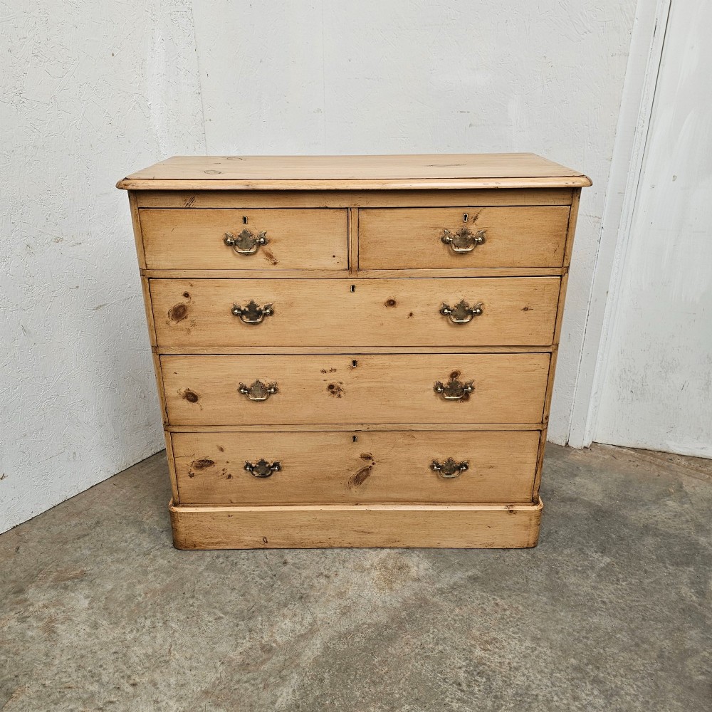 A Victorian light pine chest of drawers featuring a two-over-three drawer configuration, brass drop handles, keyholes, and a solid plinth base.