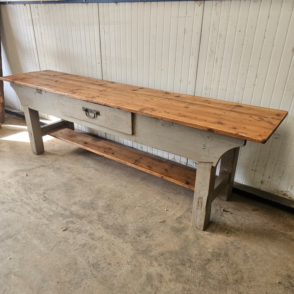 A long rustic pine worktable featuring a natural wood top, a light grey painted frame with a single drawer, and a lower shelf. View II