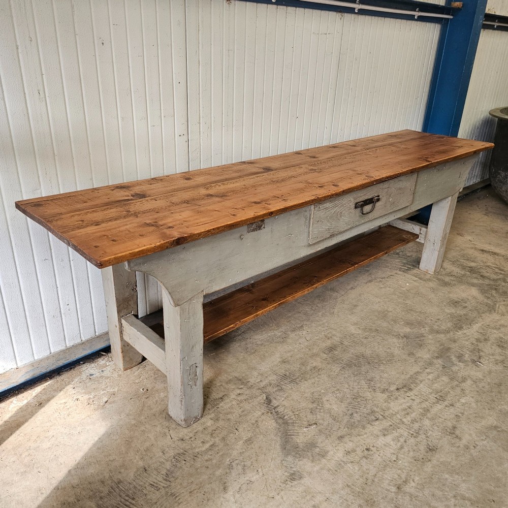 A long rustic pine worktable featuring a natural wood top, a light grey painted frame with a single drawer, and a lower shelf. View III