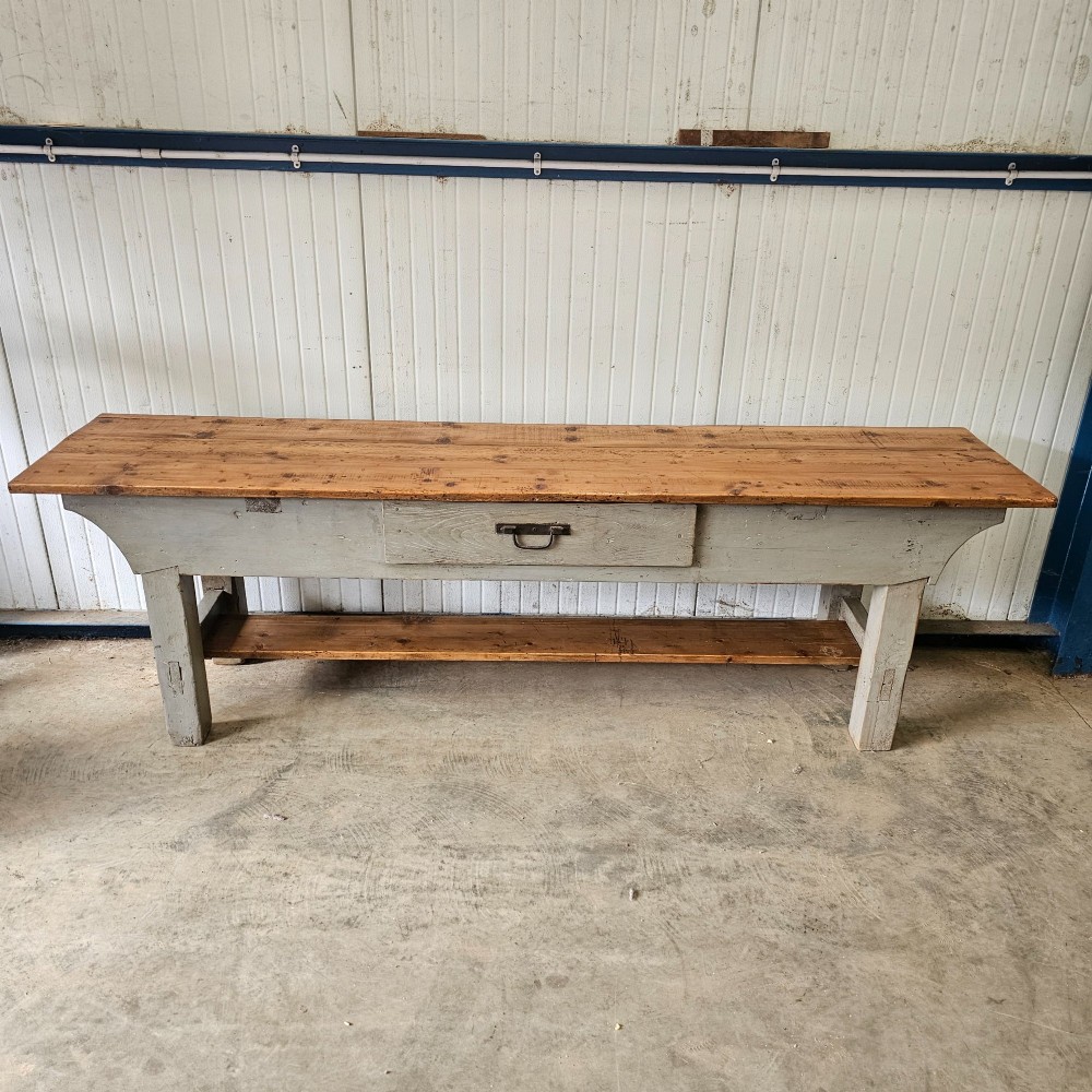A long rustic pine worktable featuring a natural wood top, a light grey painted frame with a single drawer, and a lower shelf. View IV