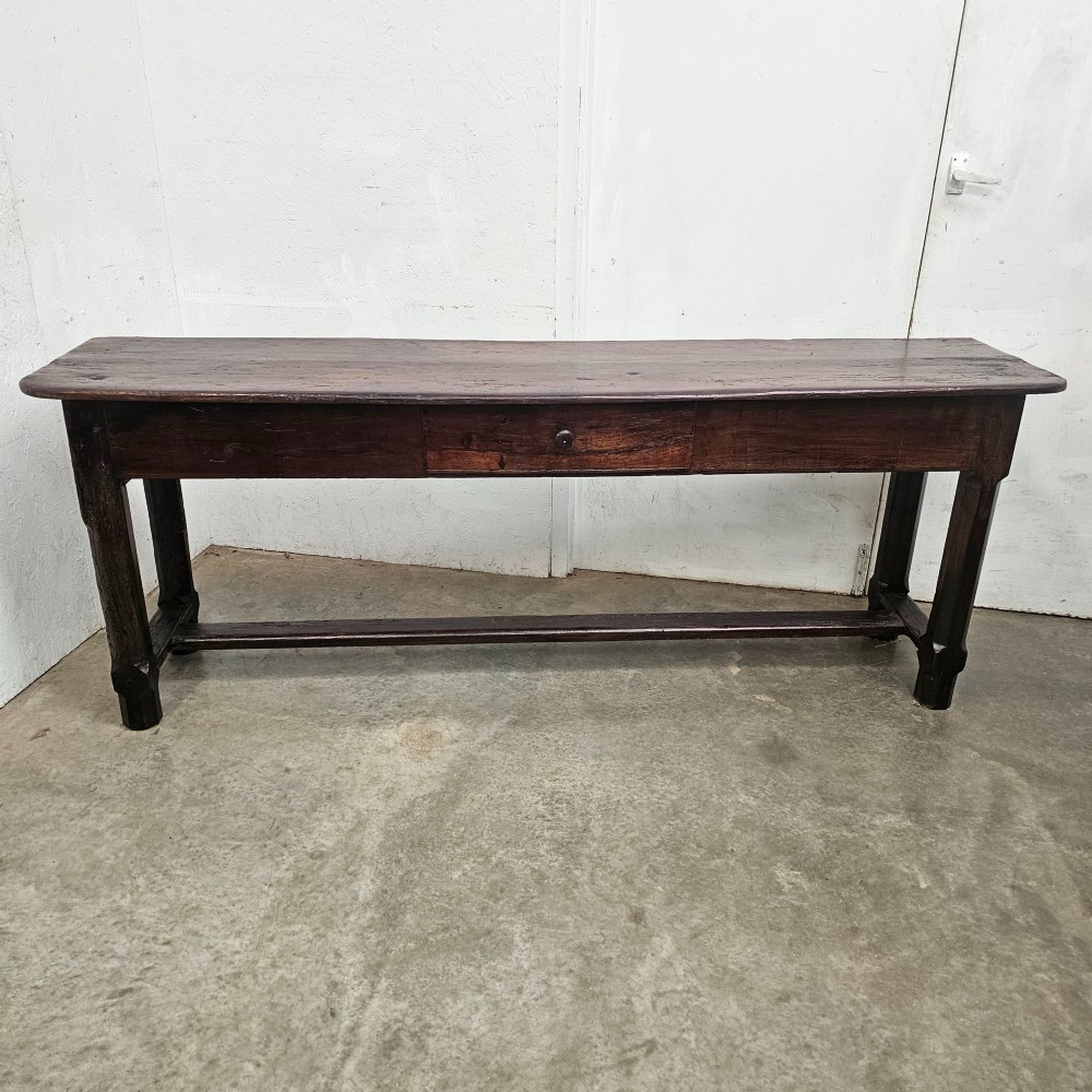 An antique dark fruitwood console table featuring a single central drawer, straight legs, and an H-stretcher base.