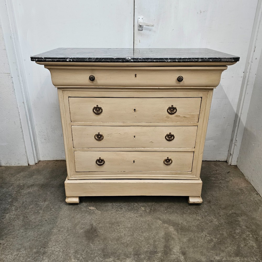 An off-white painted Louis Philippe chest of drawers with a dark marble top and brass ring handles.