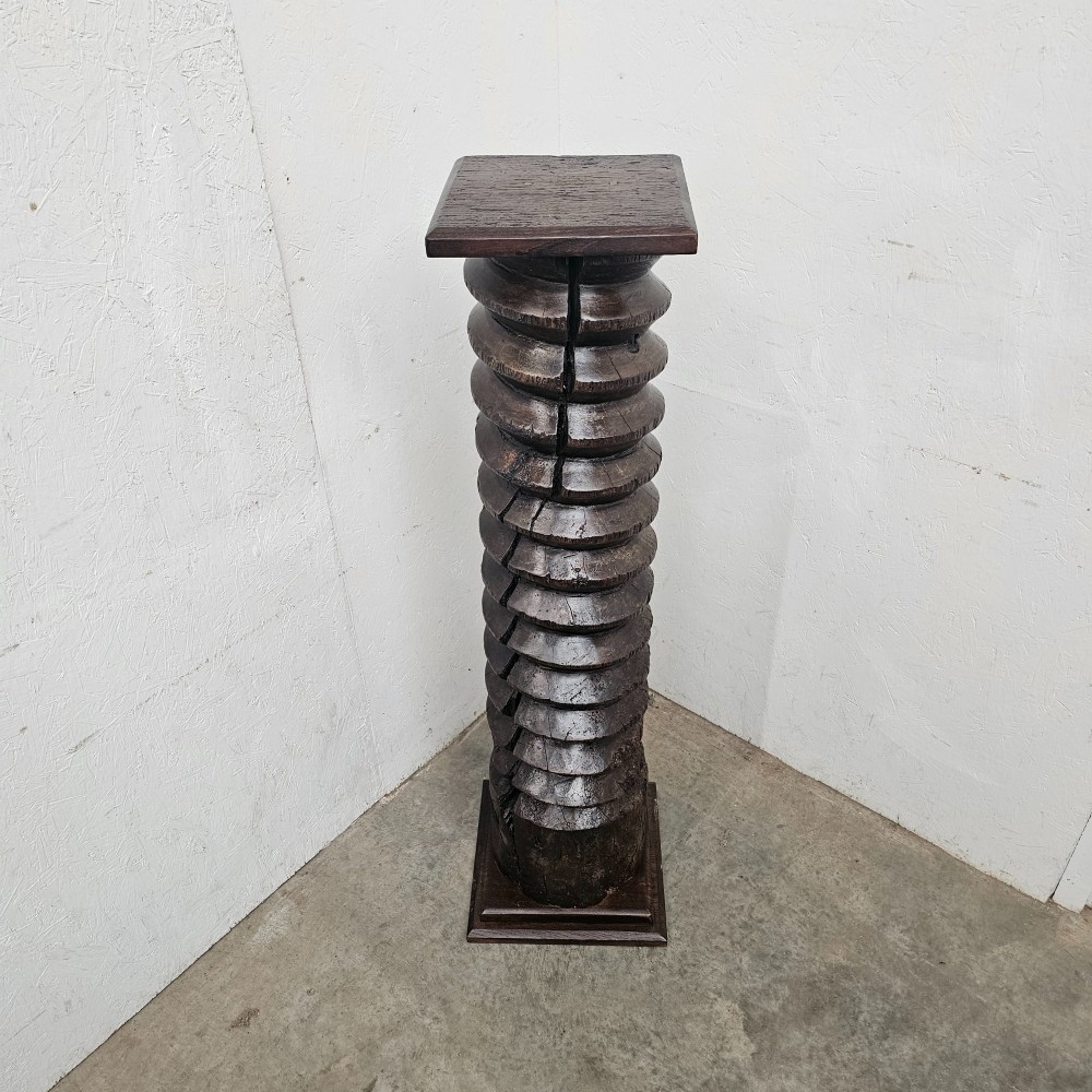 A tall hand-carved dark timber wine press screw thread with a square top and base, repurposed as a sculptural display pedestal. View IV