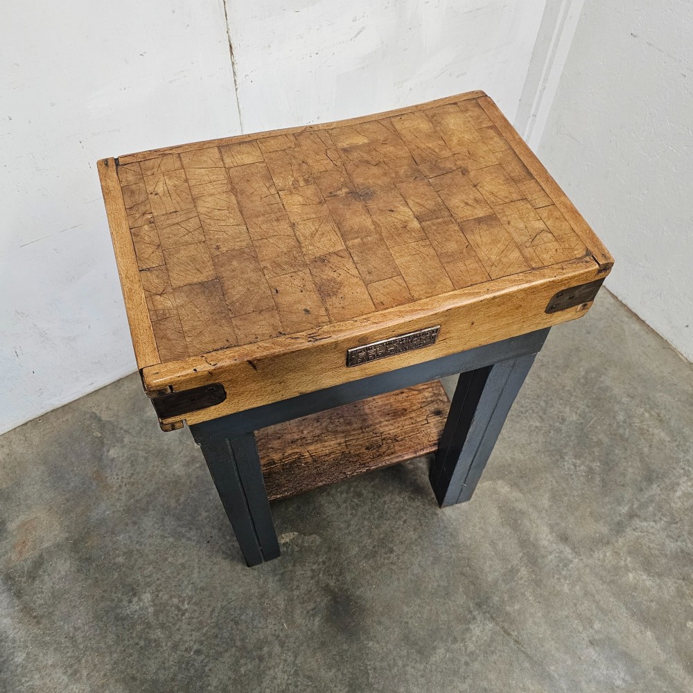 A small antique French butchers block featuring an end-grain beech top with a brass makers plate set on a dark painted wooden stand with a lower shelf. View IV