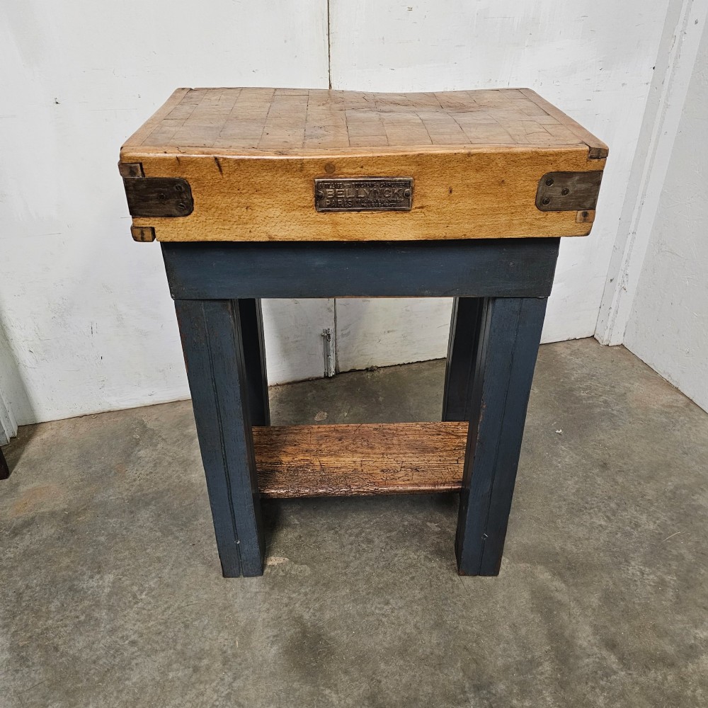 A small antique French butchers block featuring an end-grain beech top with a brass makers plate set on a dark painted wooden stand with a lower shelf.