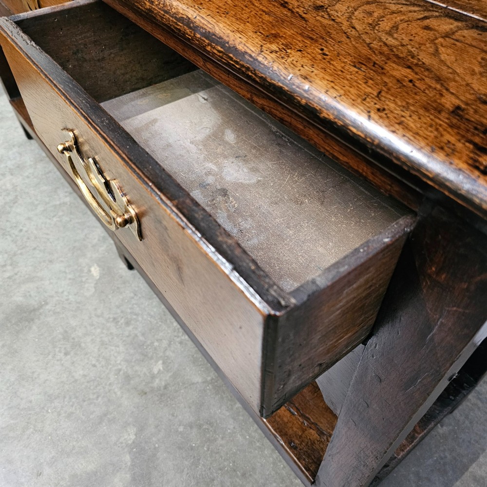 An antique dark oak potboard dresser featuring a tall open tiered plate rack over three drawer units with brass handles and a low open display shelf. View II