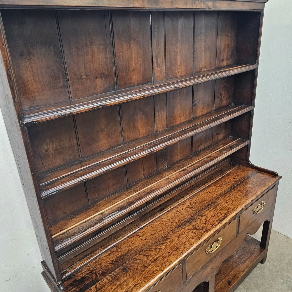 An antique dark oak potboard dresser featuring a tall open tiered plate rack over three drawer units with brass handles and a low open display shelf. View III