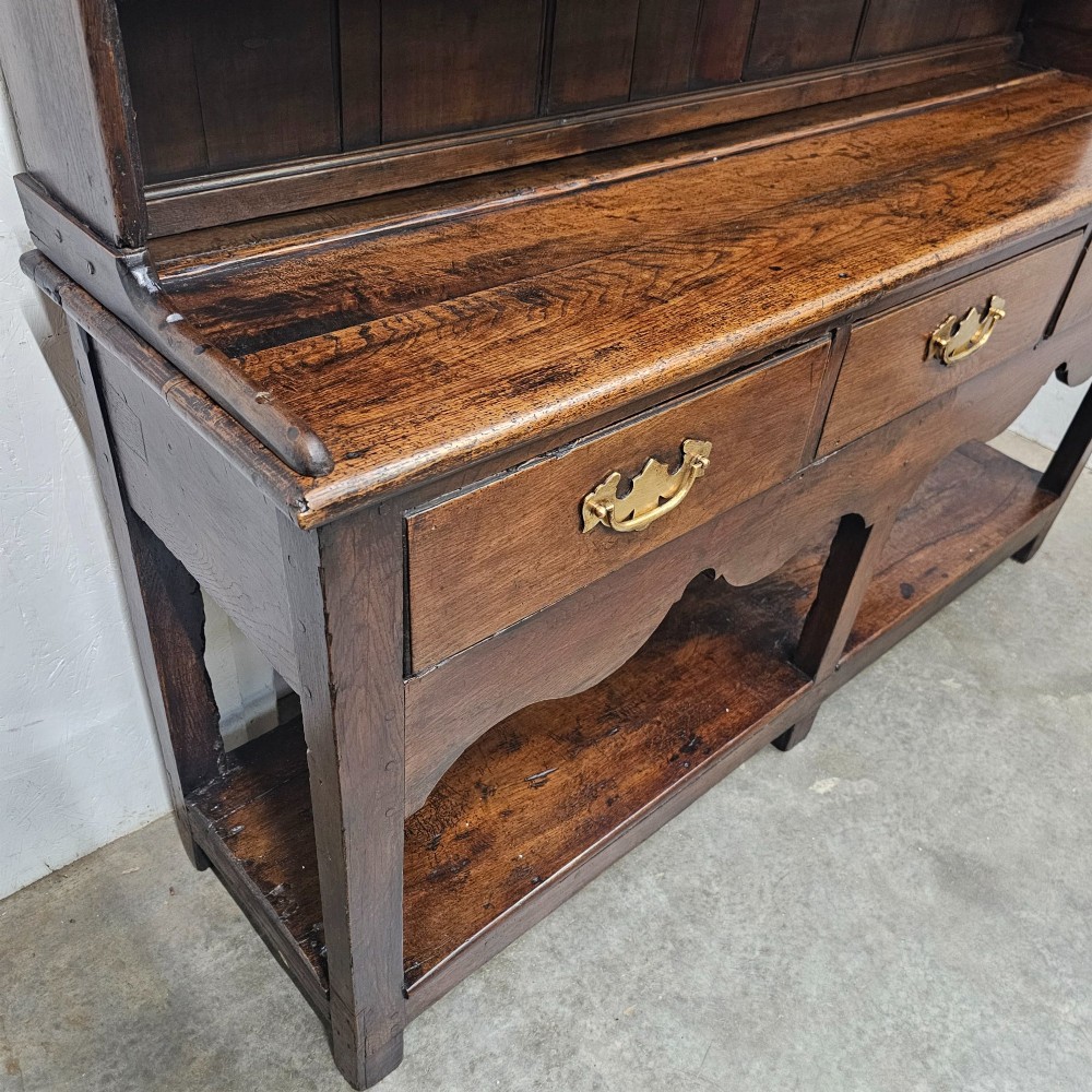 An antique dark oak potboard dresser featuring a tall open tiered plate rack over three drawer units with brass handles and a low open display shelf. View IV