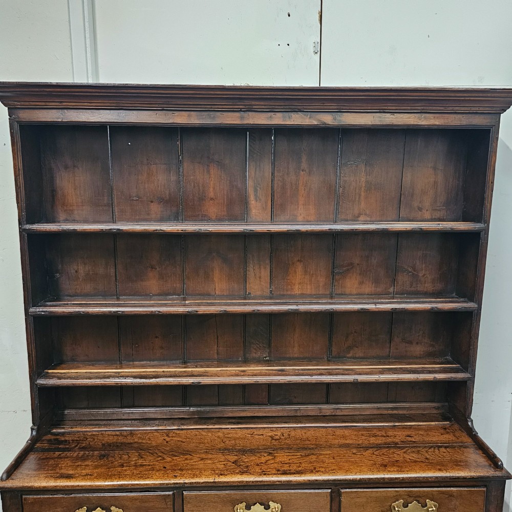 An antique dark oak potboard dresser featuring a tall open tiered plate rack over three drawer units with brass handles and a low open display shelf. View V