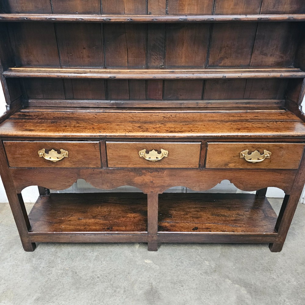An antique dark oak potboard dresser featuring a tall open tiered plate rack over three drawer units with brass handles and a low open display shelf. View VI