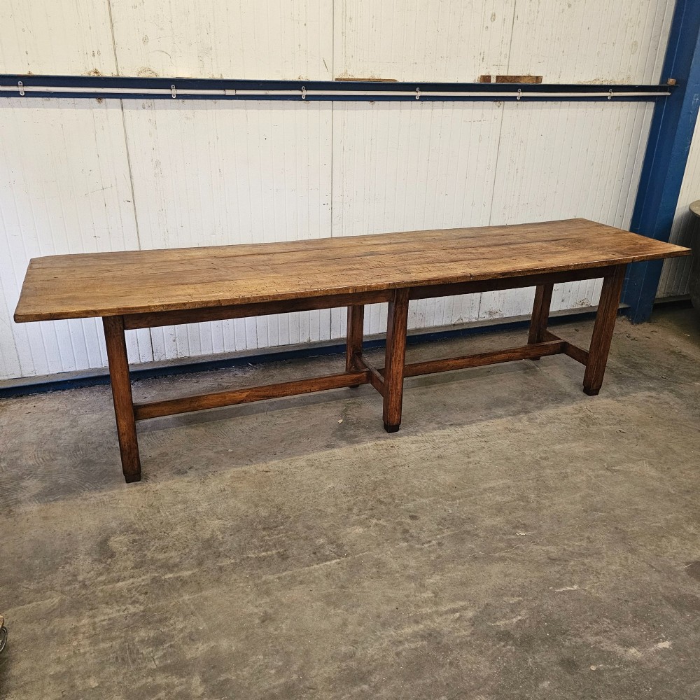 An extra long French beechwood table featuring a plank top, six square legs, and supporting stretchers in a warm brown timber finish.