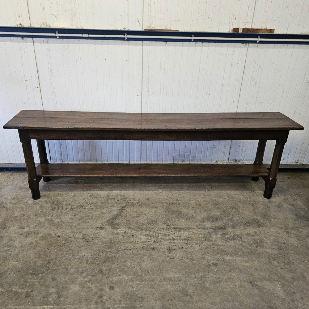 A long, narrow dark oak French serving table featuring a plank top, square legs, and a full-length lower pot shelf. View V