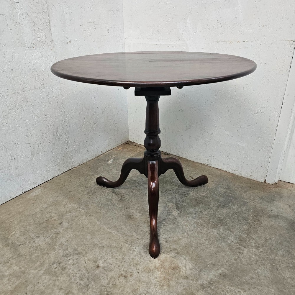 A Georgian dark mahogany wine table featuring a circular tilt-top surface supported by a turned baluster column and three cabriole tripod legs.