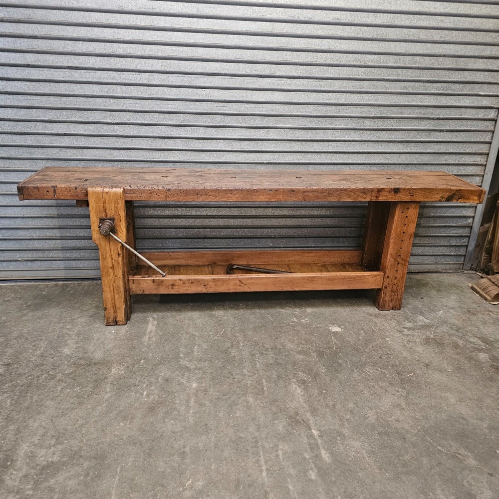 A long, heavy French oak workbench with an integrated wooden vice, lower storage shelf, and aged iron hardware. View IV