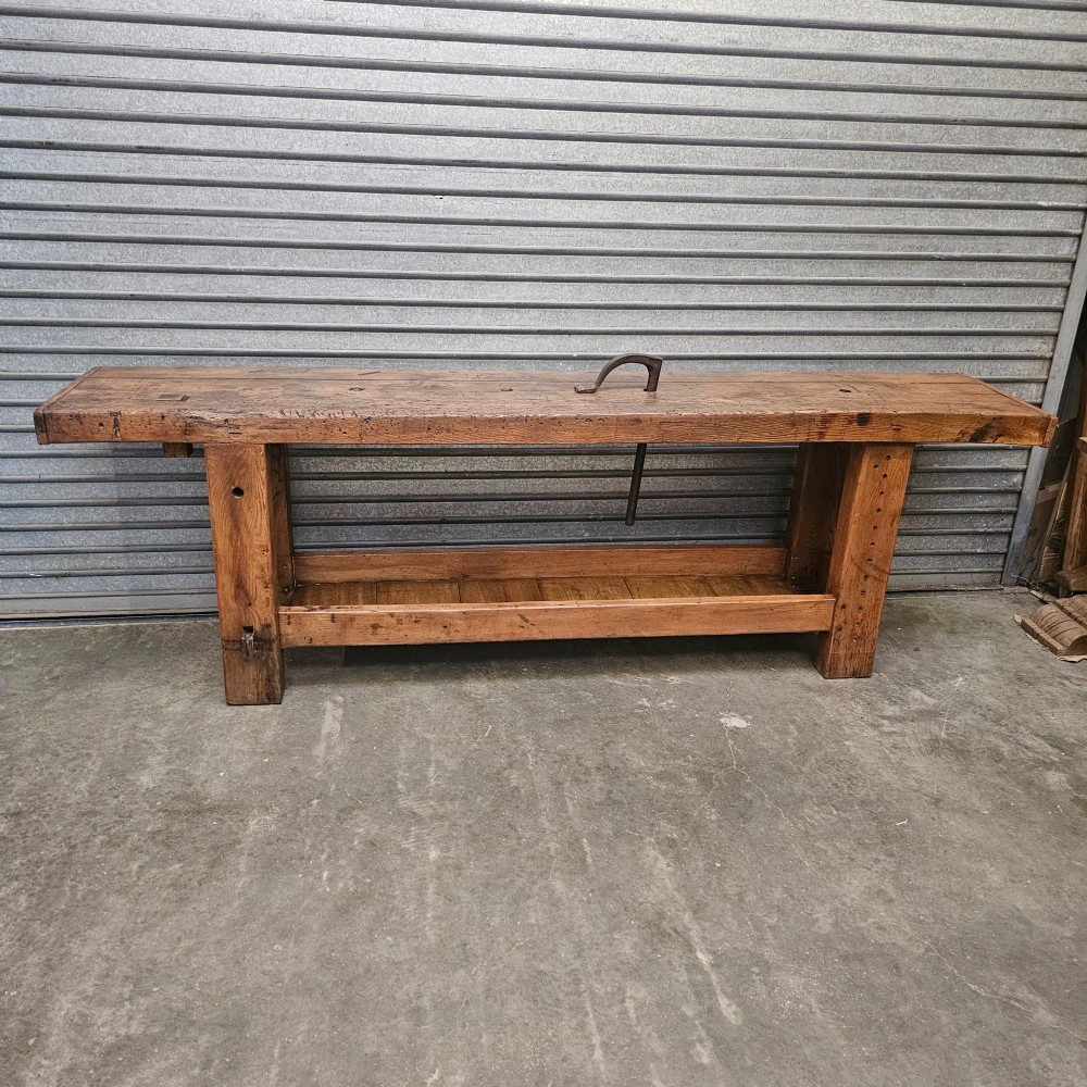 A long, heavy French oak workbench with an integrated wooden vice, lower storage shelf, and aged iron hardware. View VI