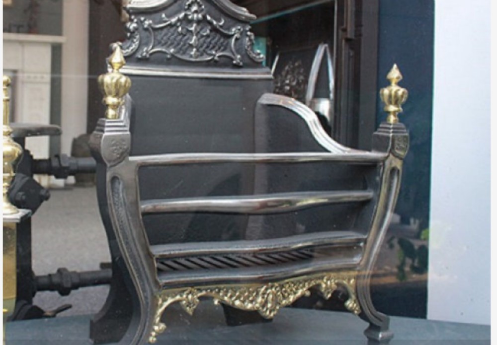 A Georgian cast iron and brass fire basket featuring urn finials, horizontal front bars, and a decorative pierced brass lower apron.