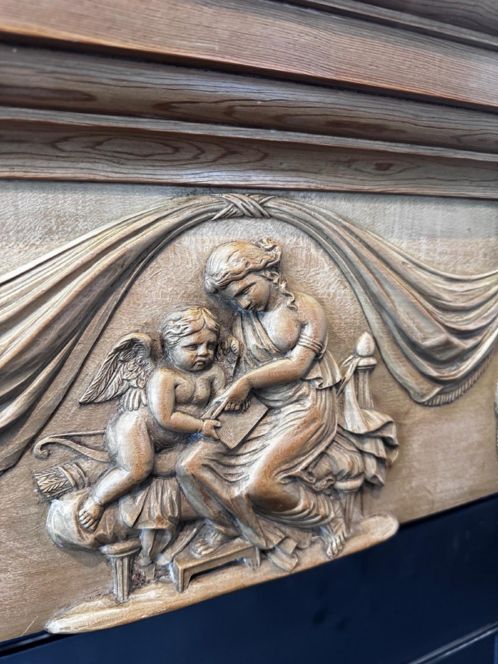 A Georgian carved wooden fireplace surround featuring a central figural relief tablet, fluted frieze, drapery swags, and classical pilasters. View VI