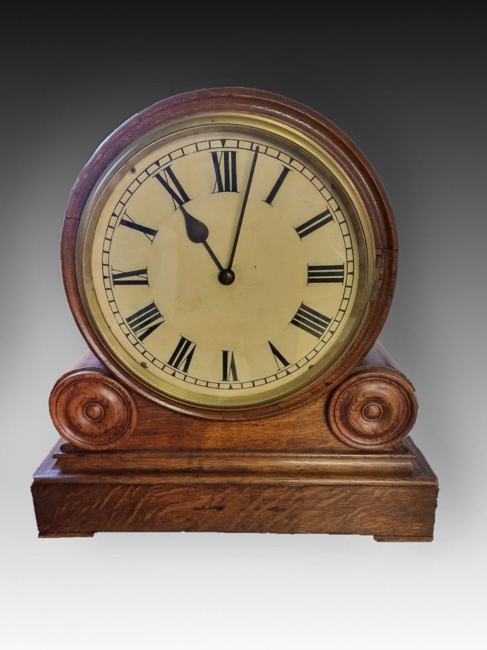 An antique wooden single fusee bracket clock featuring a round face with Roman numerals, a brass bezel, and carved scroll detailing on a plinth base.