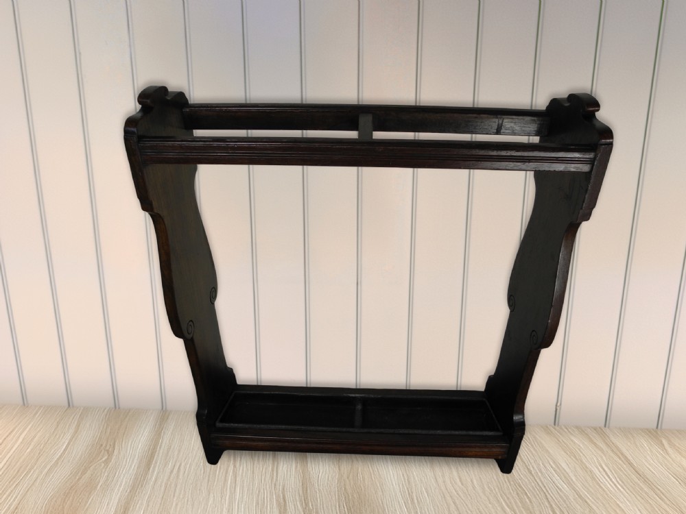 An Edwardian dark wood walking cane stand featuring a rectangular upper dividing frame, shaped side panels, and a twin-compartment drip tray at the base.