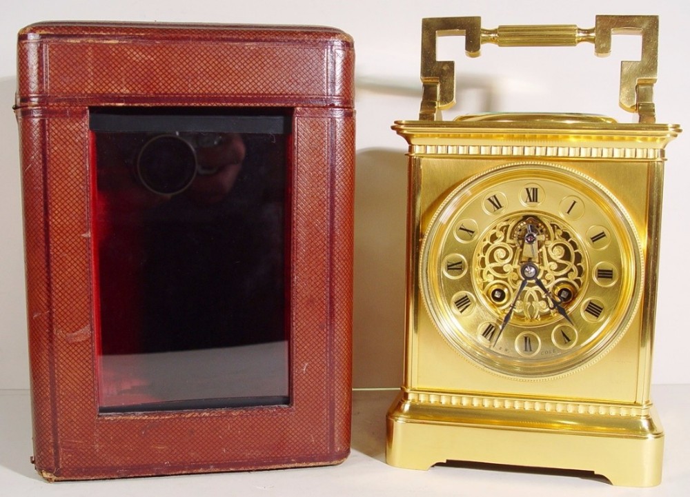 A gilded brass late 19th century French carriage clock with an openwork filigree dial standing beside its original red leather travelling case.