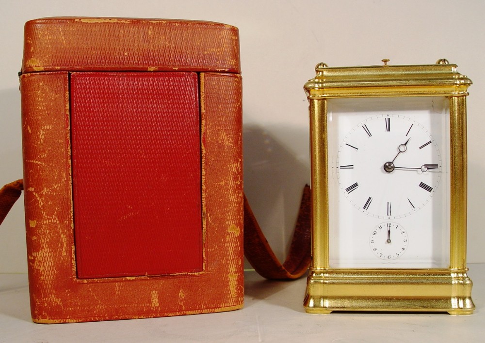 A 19th-century French gilt bronze gorge case carriage clock with a white enamel dial standing next to its red leather carrying box.