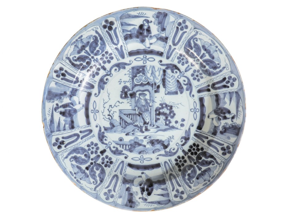 An eighteenth-century circular tin-glazed earthenware Delft plate decorated with hand-painted cobalt blue Chinoiserie figures and floral panel borders.