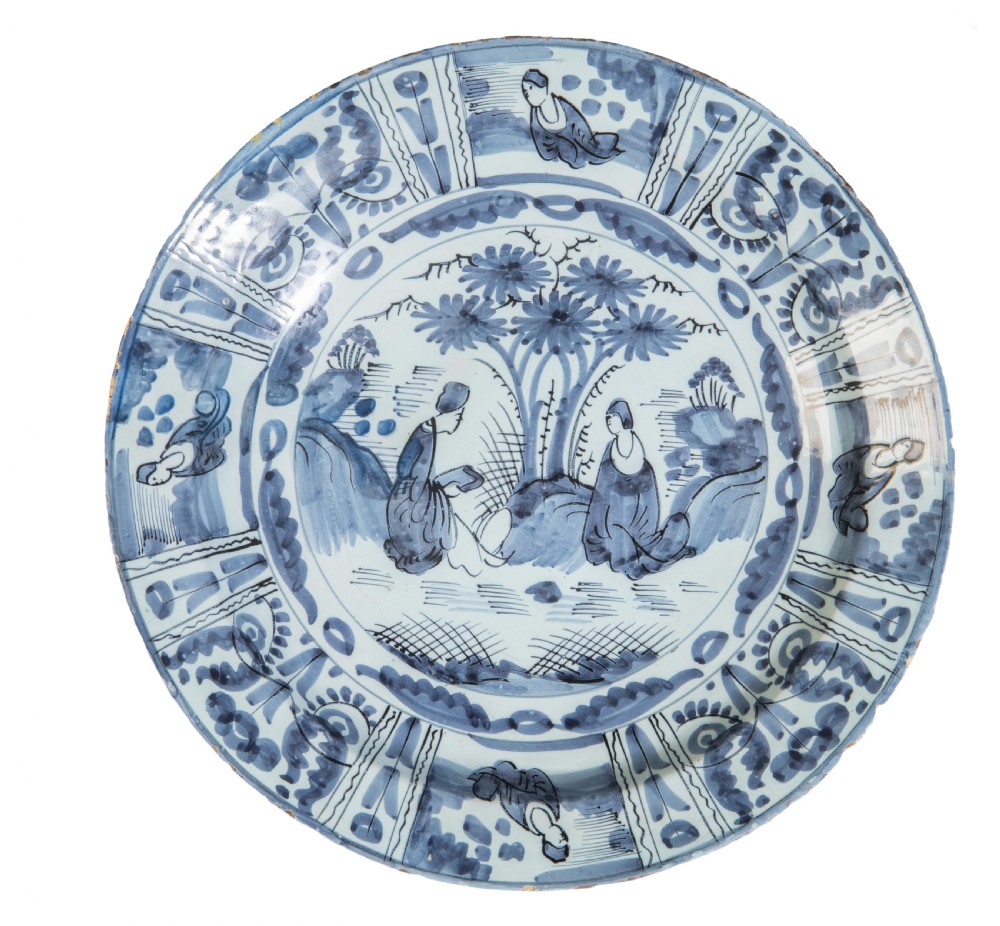 A circular 17th-century Dutch Delftware ceramic charger decorated with hand-painted cobalt blue chinoiserie scenes and panelled borders on a white tin glaze.